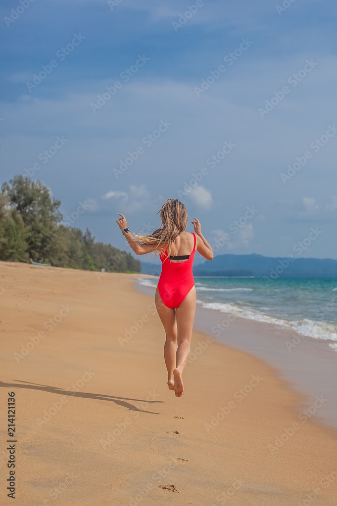 Sexy woman in red swimsuit jumping on the beach near ocean, view from the back, Phuket, Thailand