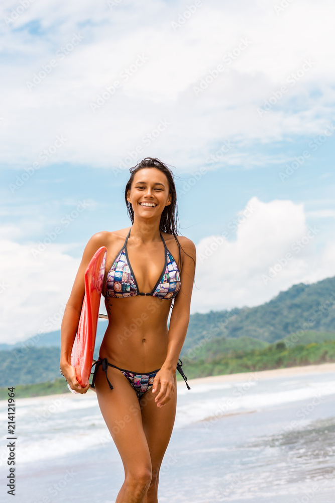 Lifestyle photo of young woman in fashion bikini with red surfboard smile  to camera. Amazing beach
