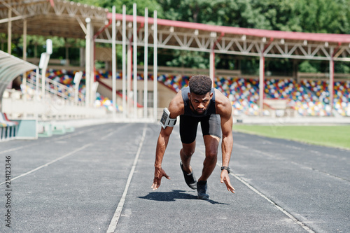 African american male athlete in sportswear racing alone down a running track at stadium.