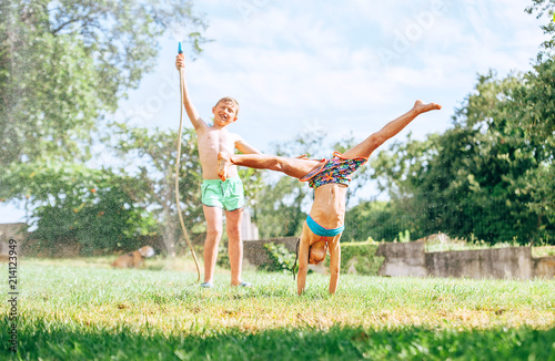 Happy children fool around in summer garden, splashing water and jumping