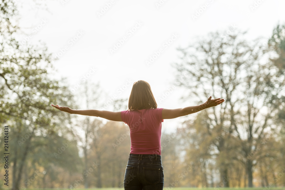 View from behind of a young woman standing in park with her arms spread widely