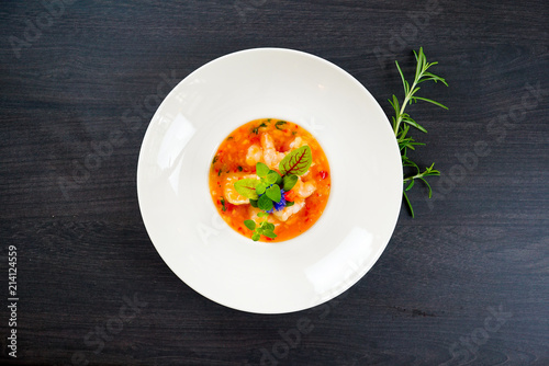 Hot Tomato soup with shrimp. Seafood creamy soup with goat cheese, olive powder, wild shrimps on bowl plate at wooden table, top view, close-up. Delicious vegetarian diet food.