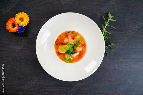 Hot Tomato soup with shrimp. Seafood creamy soup with goat cheese, olive powder, wild shrimps on bowl plate at wooden table, top view, close-up. Delicious vegetarian diet food.