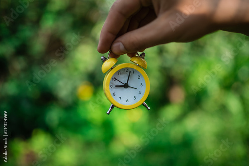 Hand with modern clock, yellow alarm clock of old style, hold in hand against green grass
