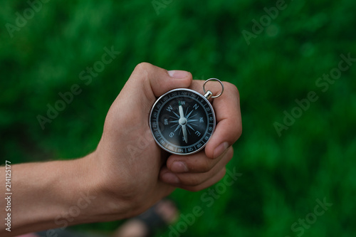 A traveler with a compass in the park. A compass in hand against a background of a blurred road. The direction of finding tourists with a compass in the forest. to get lost in the forest.