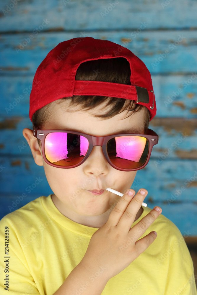 niño con gafas de sol y gorra chupando un caramelo con palo Stock Photo |  Adobe Stock