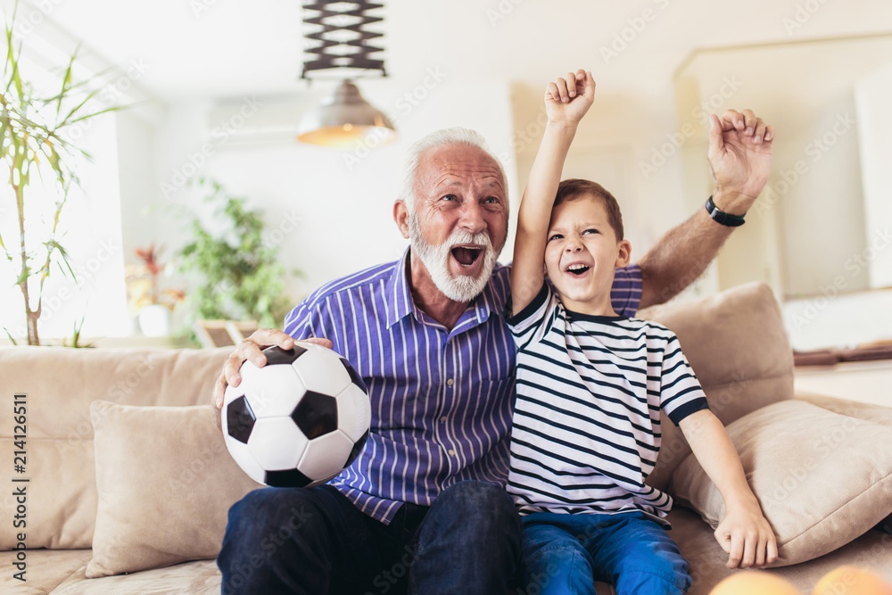 Little boy on couch with grandfather cheering for a football game