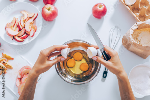 Female's hands holding eggshells cracking egg into bowl