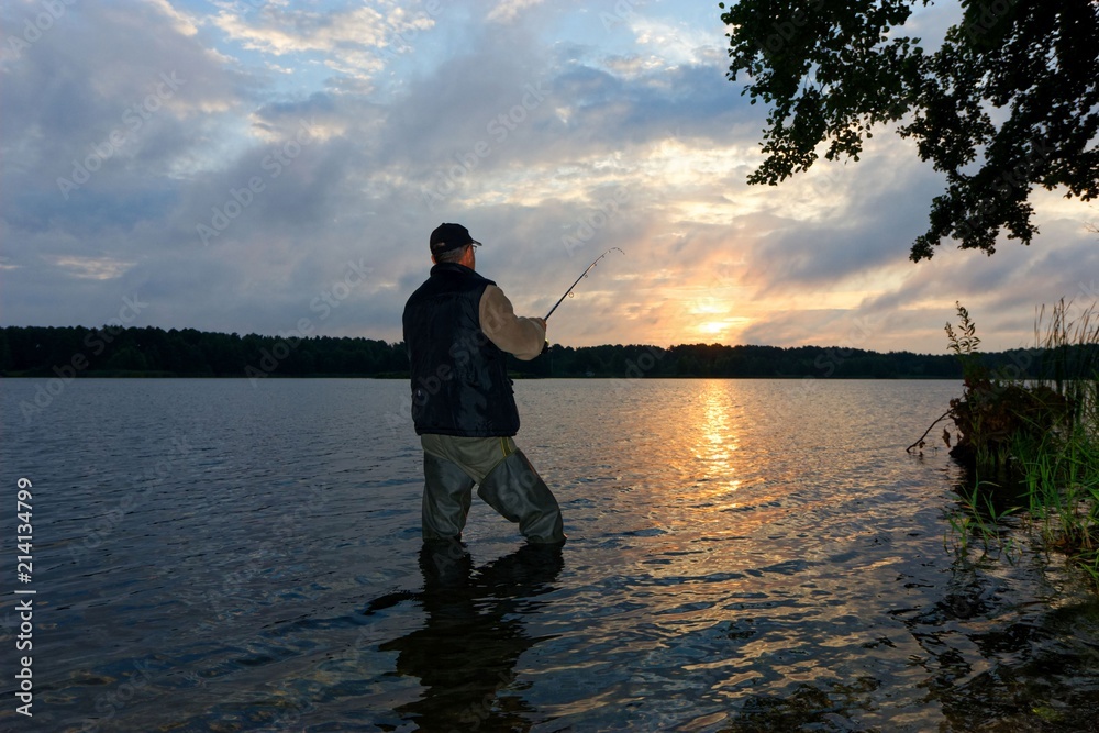 Fototapeta premium Angler catching the fish during cloudy sunrise
