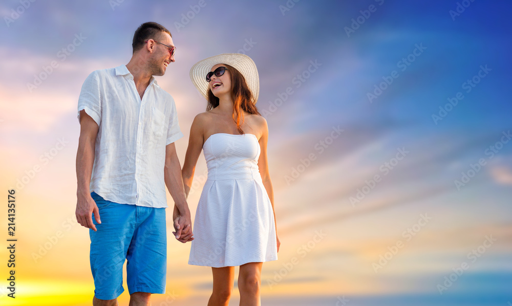 love, summer and relationships concept - happy couple on vacation wearing sunglasses and walking holding hands over evening sky background love, summer and relationships concept - happy couple on vacation wearing sunglasses and walking holding hands over evening sky background