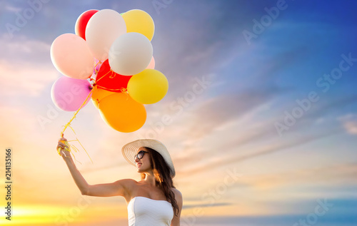 happiness  summer and people concept - smiling young woman wearing sunglasses with balloons over sunset sky background