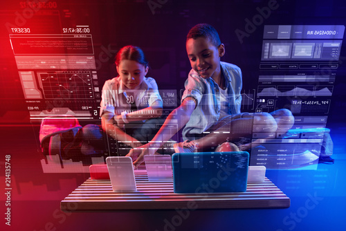 Favorite devices. Pretty girl sitting on the floor and her smiling friend taking a modern gadget and showing it photo