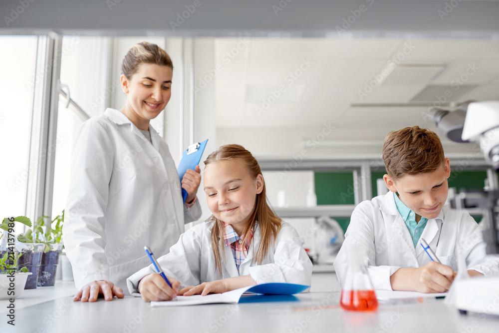 Fototapeta premium education, science and children concept - teacher and students studying chemistry at school laboratory and writing to workbooks