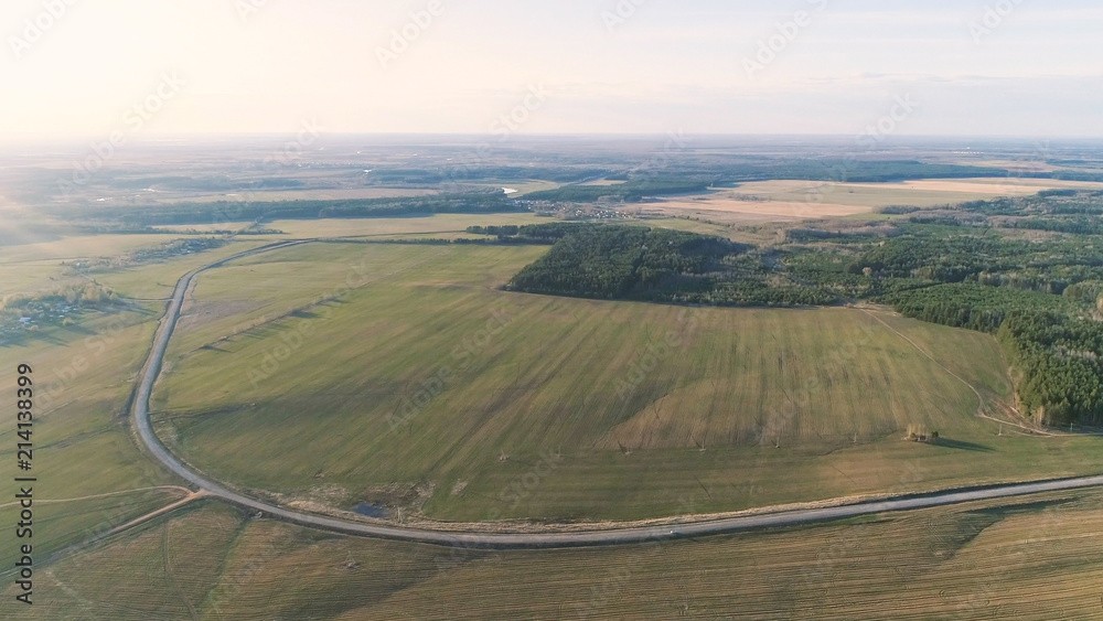 Flight above countryside green fields, forest, and village early spring, aerial panoramic view photo.