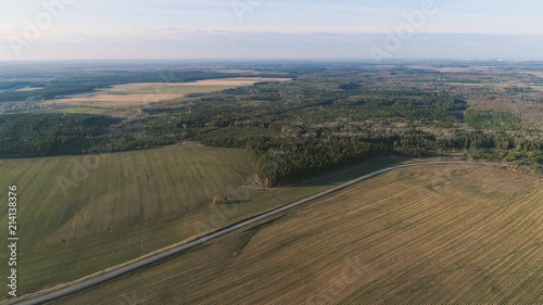 Flight above countryside green fields, forest, and village early spring, aerial panoramic view photo.