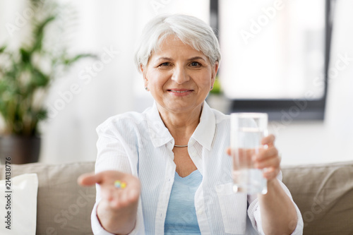 age, medicine, healthcare and people concept - senior woman with pills and glass of water at home