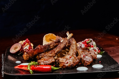 Fototapeta Naklejka Na Ścianę i Meble -  rack of lamb on a black plate decorated with pepper, pomegranate, onion and garlic