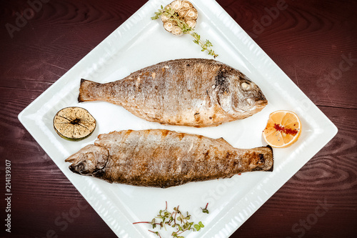 Fried fish on a wooden background. With lemons and spices. photo