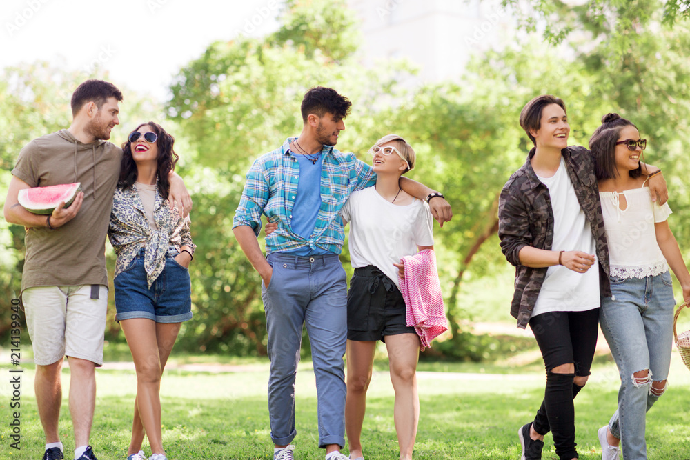 friendship and leisure concept - group of happy friends with picnic blanket and watermelon walking at summer park friendship and leisure concept - group of happy friends with picnic blanket and watermelon walking at summer park