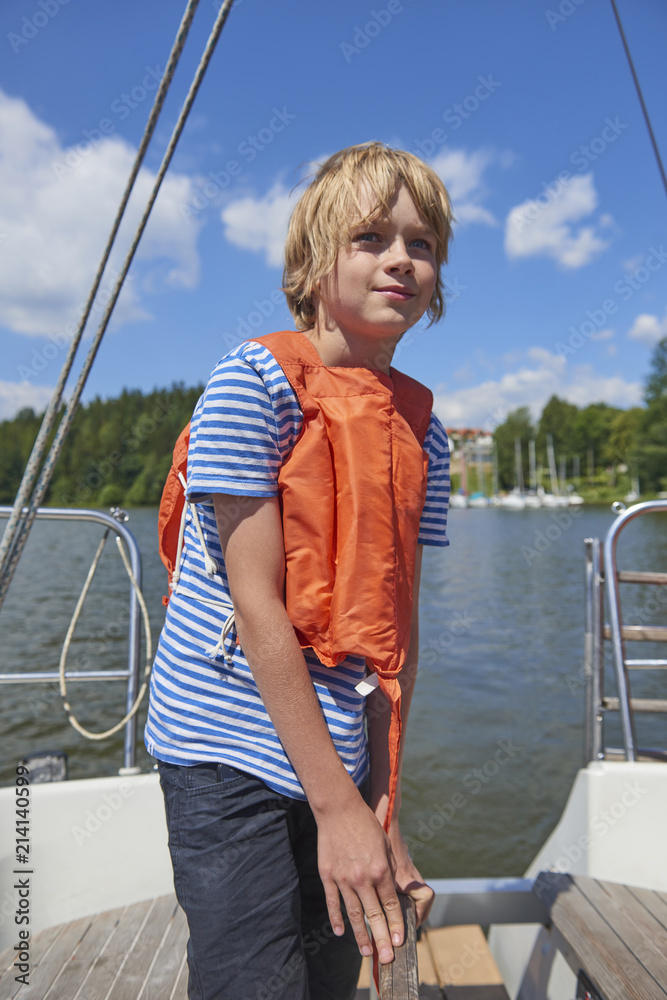 Fototapeta premium Child boy holding a yacht rudder. Cute boy captain on board of sailing yacht on summer cruise. Travel adventure, yachting with child on family vacation.