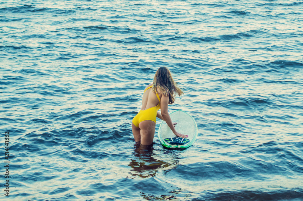 Surfer girl in a sexy yellow swim suit going out to the sea waves