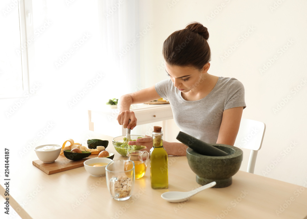 Young woman making nourishing mask with avocado in kitchen Young woman making nourishing mask with avocado in kitchen