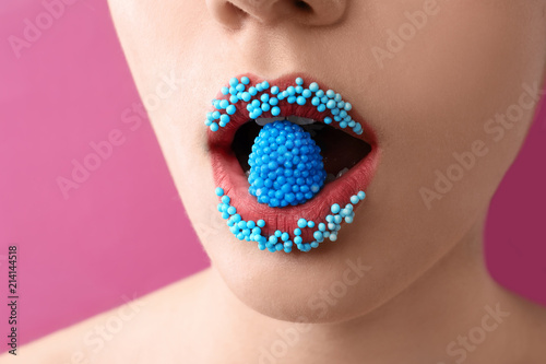 Beautiful young woman with creative makeup and candy in mouth on color background, closeup