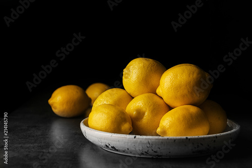 Plate with whole lemons on table against dark background