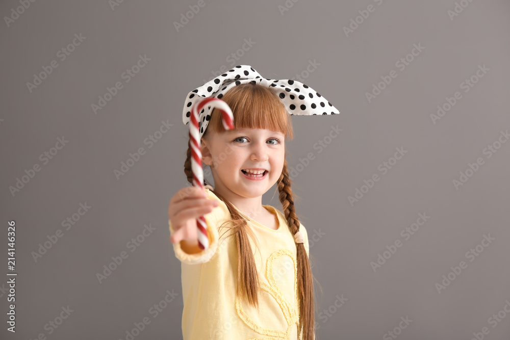 Cute little girl with candy cane on grey background