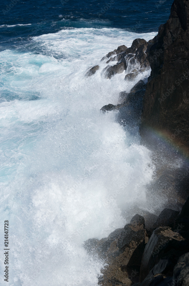 Rainbow between breaking waves in rocky coast