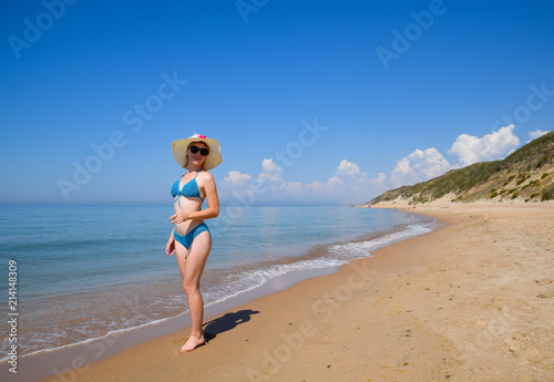 Blonde in a blue swimsuit and a white hat on the beach. Beautiful sea beach.