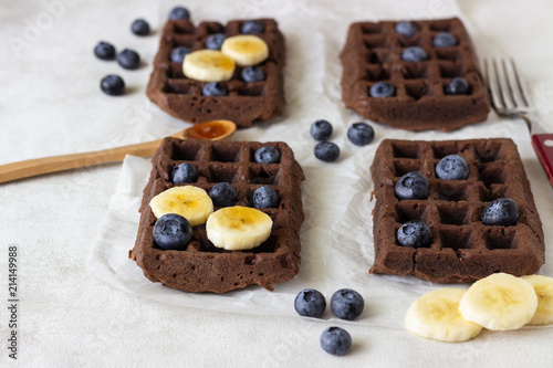 Chocolate belgian waffles with fresh blueberries, banana and honey on a white paper.