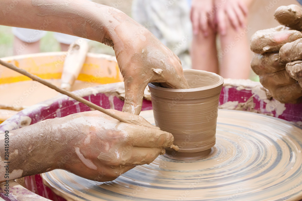 Potter's hands and the child's hand in clay over a potter's wheel. A master class on production of pottery. Modeling of clay on a potter's wheel