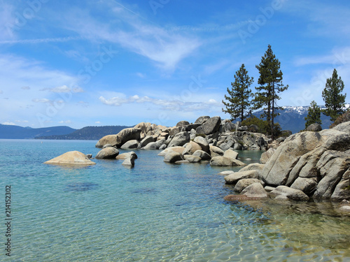 Cirrus clouds and light reams at Sand Harbor on Lake Tahoe with islands of boulders and pines, and sparkling water.