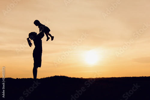Silhouette of mother and daughter lifting child in air over scenic sunset sky at riverside. relaxation time and happiness