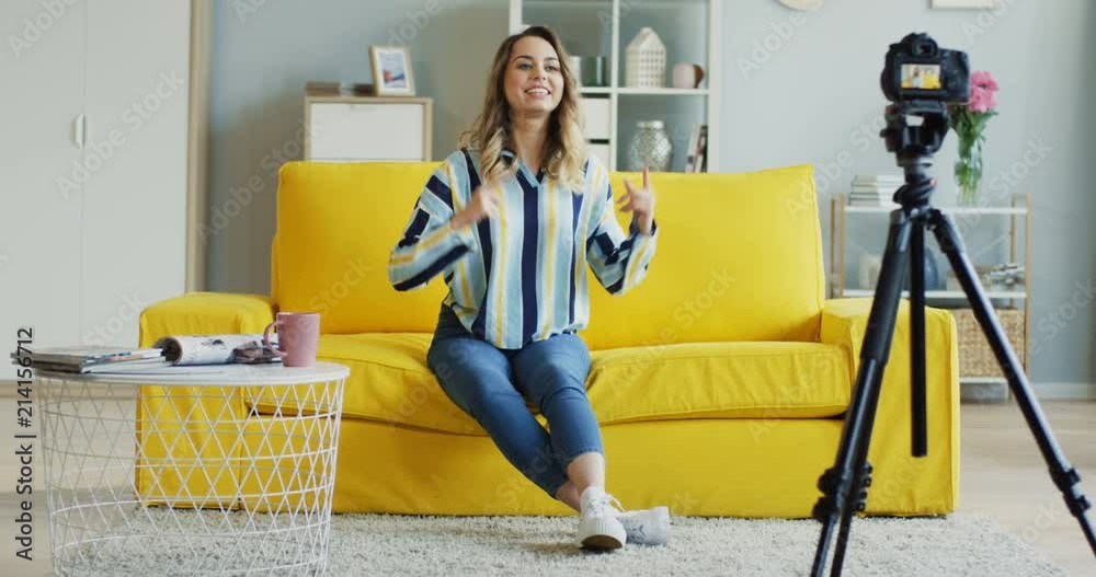 Cheerful young woman blogger recording her video blog and doing many emotionals gestures in the modern room at home. Inside.