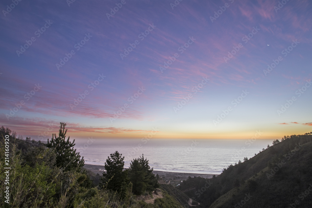 The sun goes down below a water horizon in the middle of the Pacific Ocean making a wonderful and colorful landscape with twilight at a wild beach close to Santiago de Chile city called Puertecillo