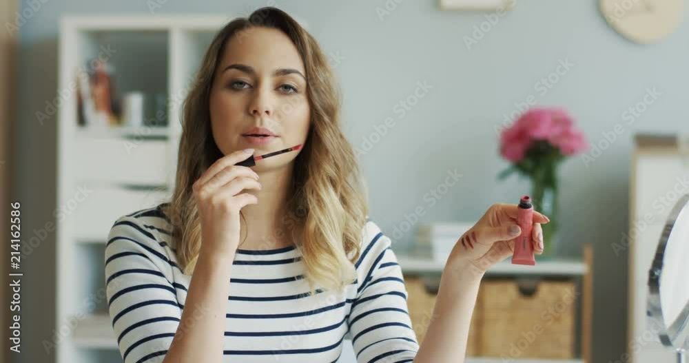 Portrait of the young beautiful woman painting her lips with lip gloss for her tutorial beauty blog video. Inside. Portrait of the young beautiful woman painting her lips with lip gloss for her tutorial beauty blog video. Inside.