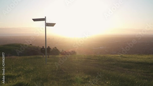 People walking up hill during sunset with cuty in background below