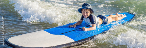 Happy baby boy - young surfer ride on surfboard with fun on sea waves. Active family lifestyle, kids outdoor water sport lessons. Summer vacation with child BANNER long format photo