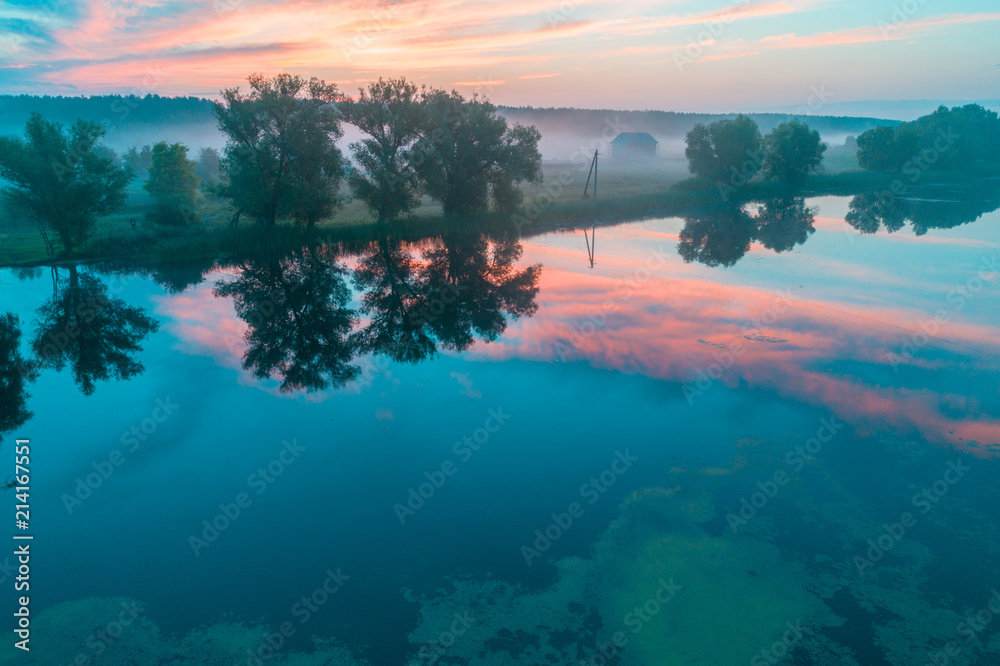 Aerial view of countryside and the lake in the early misty morning. The time before sunrise. View from above