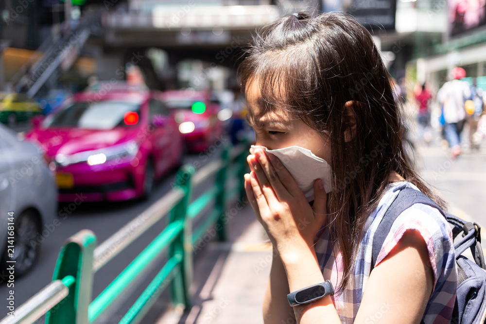 portrait of cute little girl blowing nose in paper handkerchief,Asian girl sneezing in a tissue in the city street concept of pollution,dust allergies
