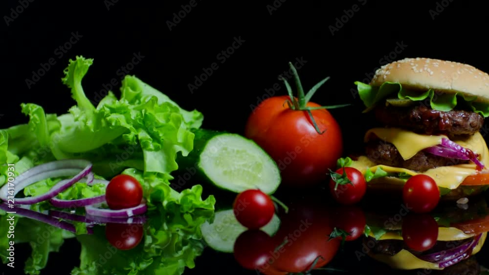 Fresh vegetables and tasty burger with cheese and beef cutlets on the black background Fresh vegetables and tasty burger with cheese and beef cutlets on the black background
