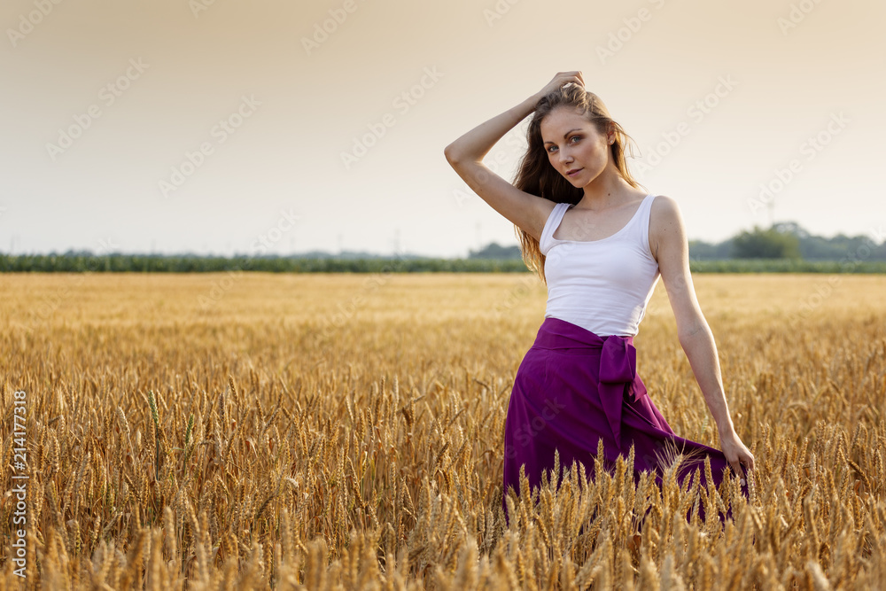 Beautiful long hair young girl standing at the wheat field at sunset Beautiful long hair young girl standing at the wheat field at sunset