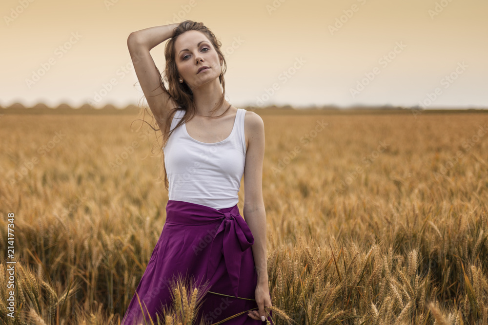 Beautiful long hair young girl standing at the wheat field at sunset Beautiful long hair young girl standing at the wheat field at sunset