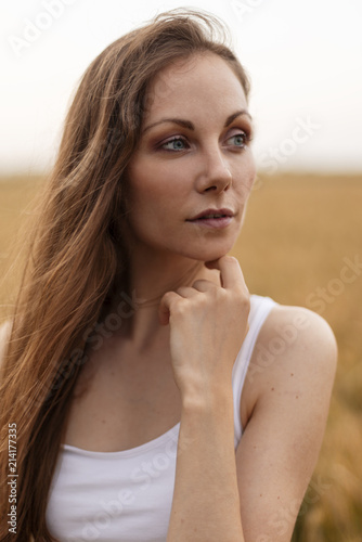 Beautiful long hair young girl standing at the wheat field at sunset