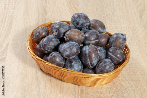Brown basket full of ripe plums on a wooden table