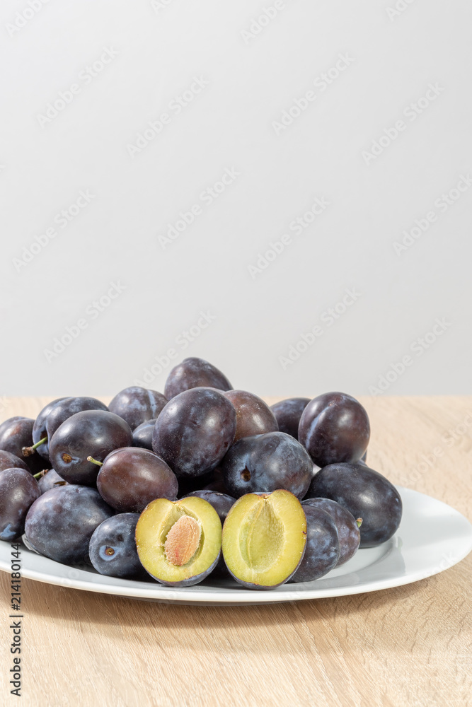 Halved plum with several ripe plums on a white plate in the kitchen Halved plum with several ripe plums on a white plate in the kitchen