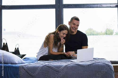 cute woman and man watching together laptop near window in room