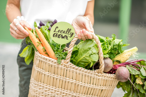 Holding bag full of fresh organic vegetables with green sticker from the local market on the green background photo